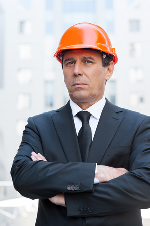 Confident contractor. Confident mature man in formalwear and hardhat keeping arms crossed and looking at camera while standing outdoorsの写真素材