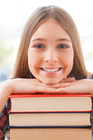 Smart and confident . Cheerful teenage girl leaning at the book stack and smilingの写真素材
