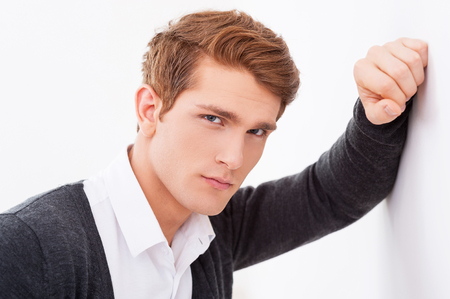 Confident handsome. Handsome young man leaning at the wall and looking at cameraの写真素材