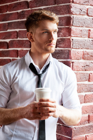 Having a coffee break. Handsome young man in shirt and tie holding coffee cup and looking through the windowの写真素材