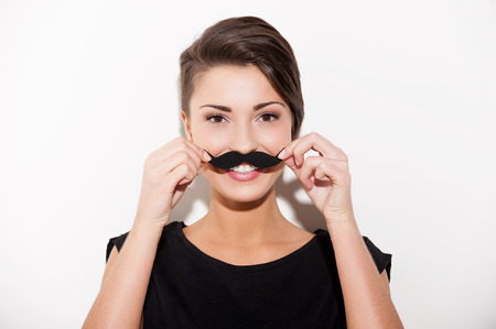 Just having fun. Beautiful young short hair woman holding fake mustache on her face and smilingの写真素材