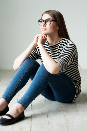 Beauty day dreaming. Beautiful young woman in striped clothing sitting on the floor and looking awayの写真素材