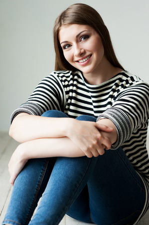 Casual beauty. Beautiful young woman in striped clothing sitting on the floor and smiling の写真素材