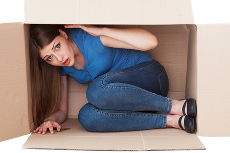 This box is too small. Shocked young woman looking at camera while sitting in a cardboard boxの写真素材