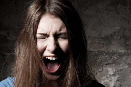 Terrified woman. Terrified young woman keeping eyes closed and shouting while standing against dark...