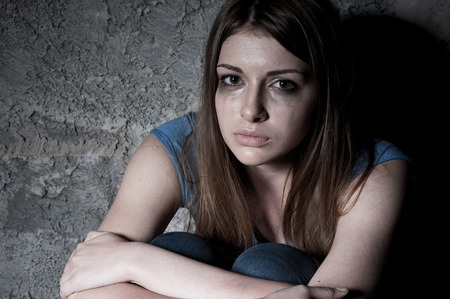 Hopelessness  Top view of young woman crying and looking at camera while sitting against dark wallの写真素材