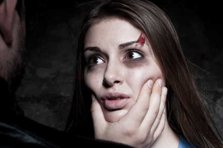 Face to face with her torturer  Young beaten up woman crying and looking at the man standing in front of her and touching her face の写真素材