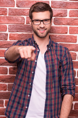 I choose you! Handsome young man pointing you and smiling while standing against brick wall の写真素材