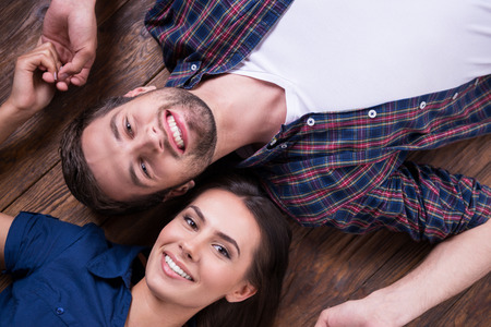 Happy to be together. Top view of beautiful young loving couple lying together on the hardwood floor and holding hands の写真素材