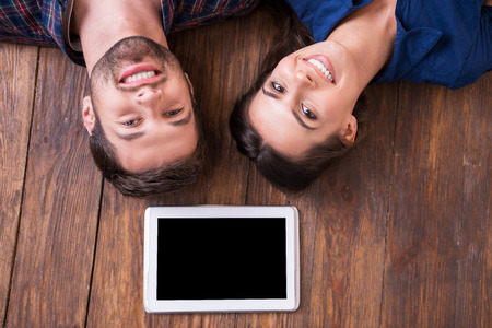 Digital age couple. Top view of beautiful young loving couple lying together on the hardwood floor and holding hands の写真素材