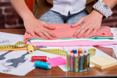 Close-up of tailor adjusting a stack of multi colored textile laying on the table with other sewing...