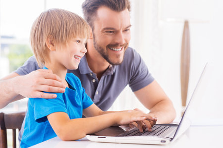 Little IT genius. Happy father and son looking at the laptop while little boy typing something on...