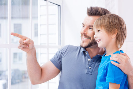 Just look over there! Happy father and son standing near the window while father pointing away and smilingの写真素材