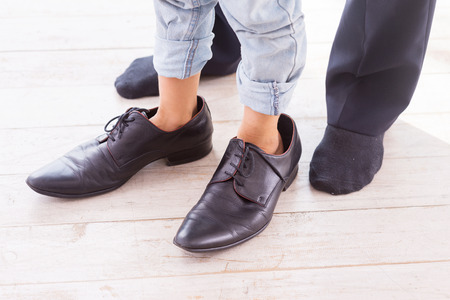 Close-up of child wearing large shoes while his father standing in socks near him の写真素材