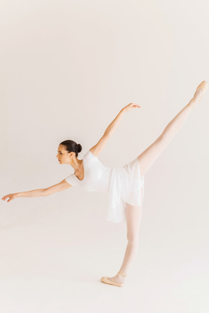 Skill and grace. Full length side view of beautiful young ballerina in white tutu dancing against white backgroundの写真素材
