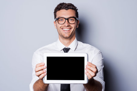 Copy space on his tablet. Handsome young man in shirt and tie showing his digital tablet and smiling...