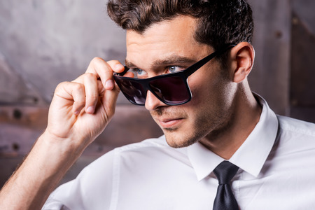 Cool and handsome. Confident young man in shirt and tie adjusting his sunglasses and looking away while standing against metal backgroundの写真素材