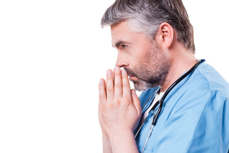 Doctor praying. Side view of mature grey hair doctor holding hands clasped near face while standing...