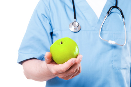 Fruits make you healthy. Close-up of surgeon in blue uniform holding green apple while standing isolated on whiteの写真素材