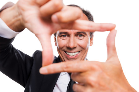 Focusing at you. Cheerful mature man in formalwear gesturing finger frame and looking through it...