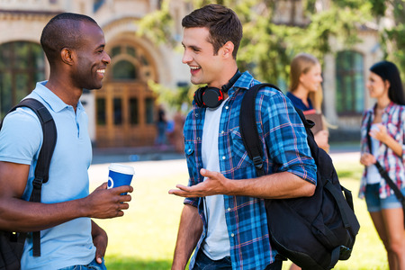Chatting with friends. Two young men talking to each other and smiling while two women standing in the backgroundの写真素材