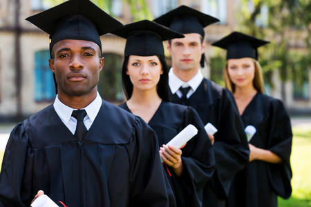 Feeling confident about their future. Four college graduates standing in a row and looking at cameraの写真素材