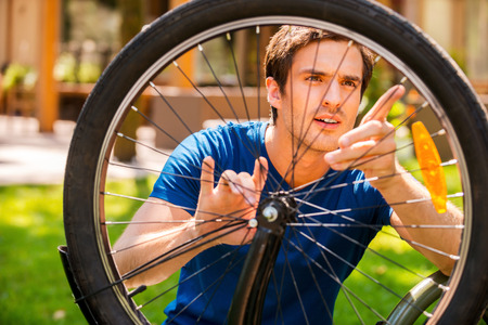 Fixing my bike. Confident young man fixing his bike while standing outdoors and against houseの写真素材