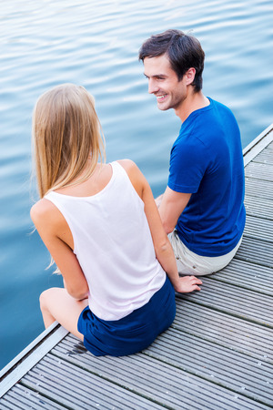 Spending good time together. Top view of beautiful young loving couple sitting at the quayside together and looking at each other with smileの写真素材