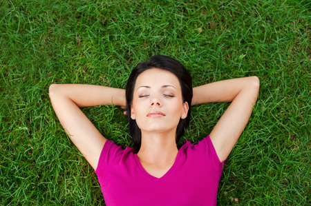 Total relaxation. Top view of beautiful young woman sleeping while holding hands behind head and lying on the green grassの写真素材