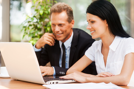 Working on project together. Two business people in formalwear looking at laptop and smiling while sitting outdoors togetherの写真素材