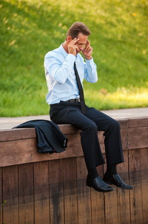 Depressed businessman. Depressed mature businessman holding head in hands while sitting at the quayside の写真素材