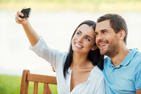 Selfie! Beautiful young loving couple sitting on the bench together and making selfie with mobile phoneの写真素材