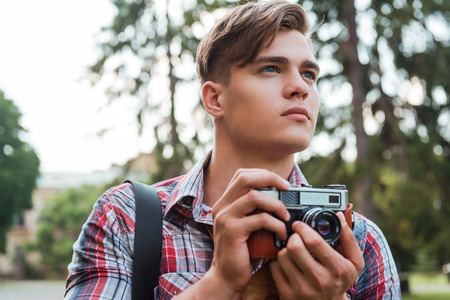 Just inspired. Handsome young man holding digital camera and looking away while standing outdoorsの写真素材