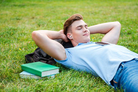 Finding a peaceful place to relax. Handsome young man holding hands behind head and smiling while lying on grass and listening to MP3 Playerの写真素材