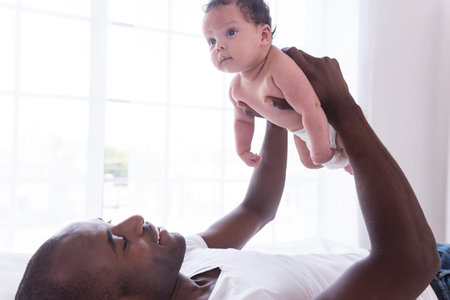 Proud and happy father. Side view of happy young African man lifting up his little baby boy and...