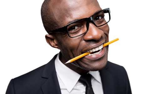 Smart and creative. Playful young African man in formalwear holding pencil in mouth and smiling while standing isolated on white backgroundの写真素材