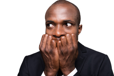 Terrified businessman. Terrified young African man in formalwear holding fingers in mouth and looking away while standing isolated on white backgroundの写真素材
