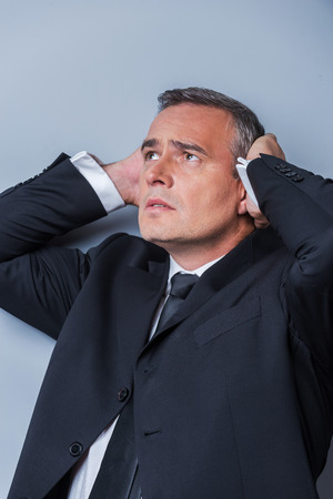 Oh my god! Frustrated mature man in formalwear holding head in hands and looking up while standing against grey backgroundの写真素材