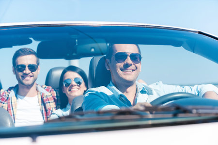 We love traveling together! Group of young happy people enjoying road trip in their white...