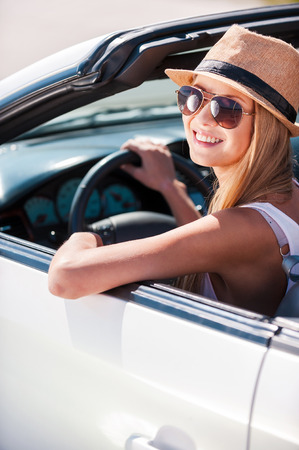 Beauty in convertible. Beautiful young funky woman in sunglasses sitting on front seat of her convertible and smiling の写真素材