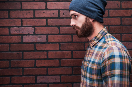 Confident handsome. Side view of handsome young bearded man standing against brick wallの写真素材