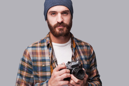Confident photographer. Handsome young bearded man holding old-fashioned camera and looking at...