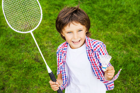 Little champion. Top view of happy little boy holding badminton racket and shuttlecock while standing on green grassの写真素材