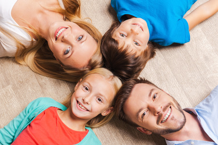 Happy family. Top view of happy family of four bonding to each other heads and smiling while lying on the hardwood floorの写真素材