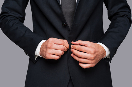 Making business look good. Close-up of man buttoning his jacket while standing against grey backgroundの写真素材