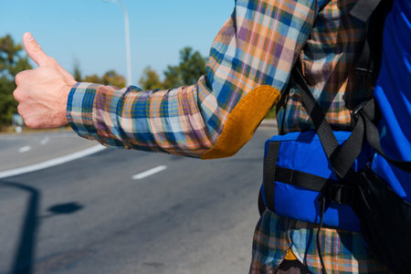 Now is time to take a ride. Close-up of young man carrying backpack stretching out hand with thumb...