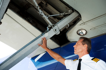 Checking the wing. Low angle view of confident male pilot in uniform examining airplane wingの写真素材
