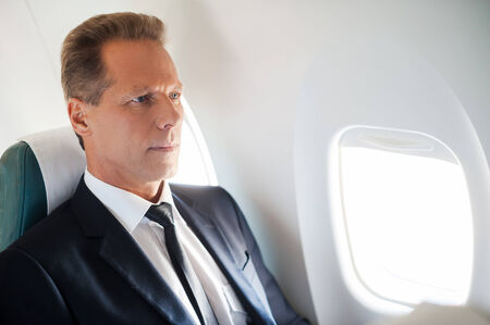 Business travel. Confident mature businessman sitting at his seat in airplaneの写真素材