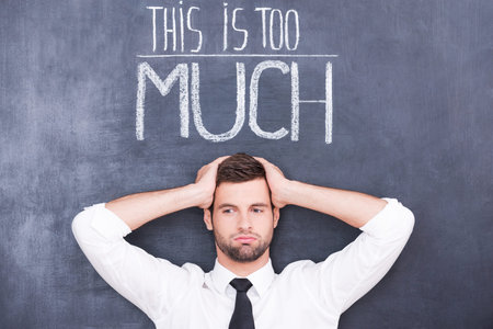 Just can not stand! Confused young man standing against chalkboard with hands on his head