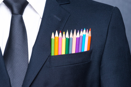 Multicolored businessman.  Close-up of a pocket of businessman with colorful pencils while standing against blackboardの写真素材